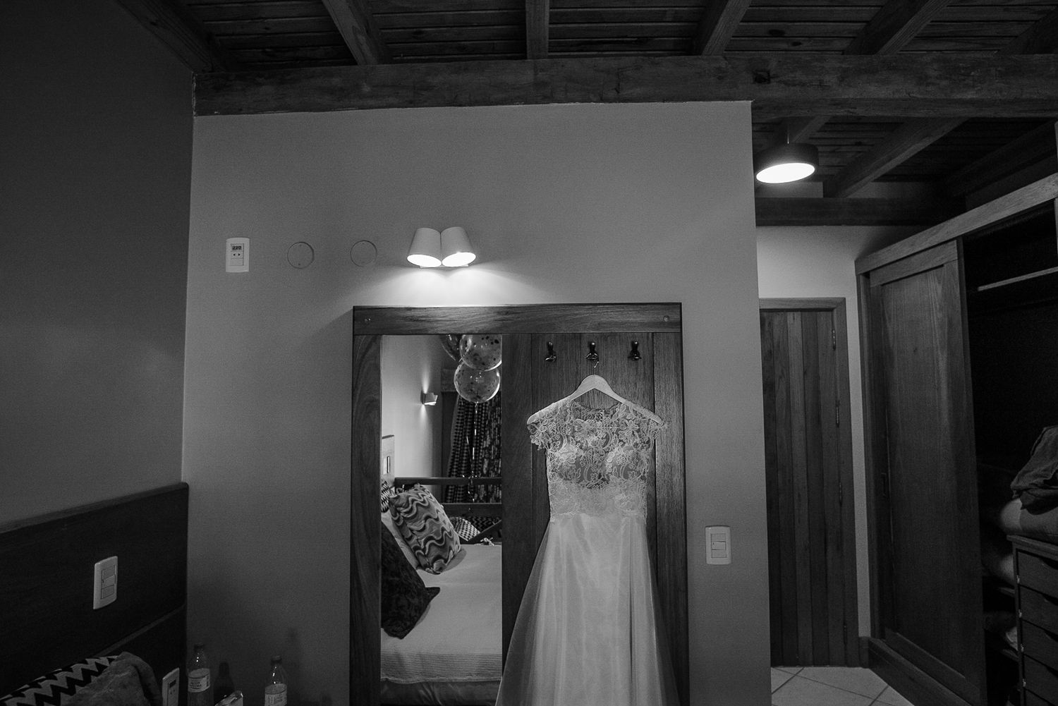 A wedding dress hangs in a dimly lit room with dramatic lighting and shadows.
