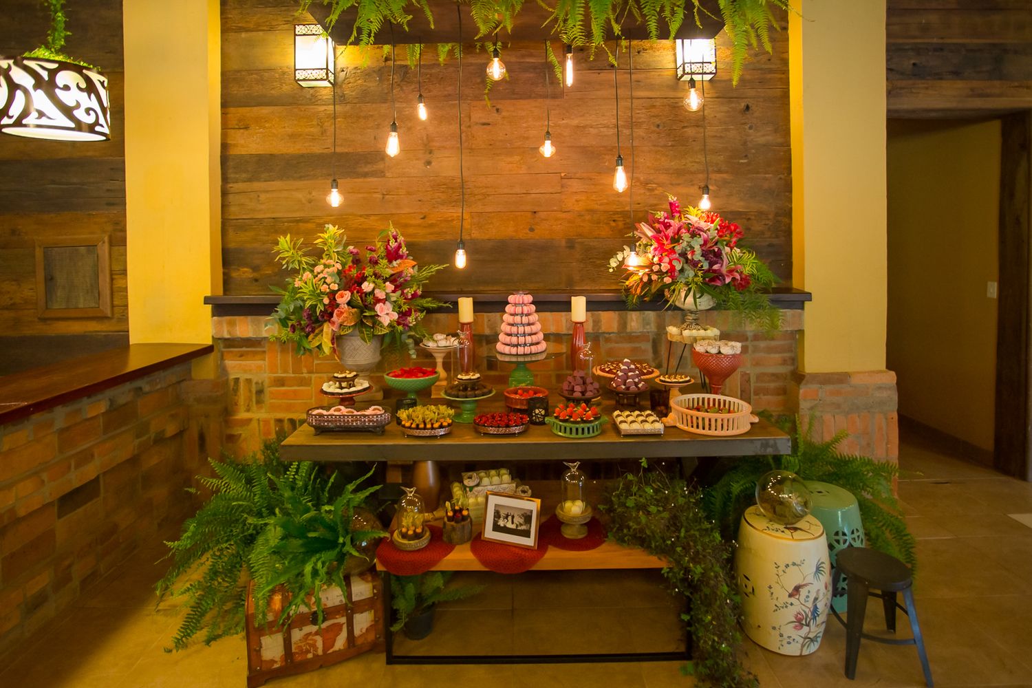 Elegant dessert display featuring a tiered cake, pastries, and floral arrangements on wooden shelving with warm lighting.