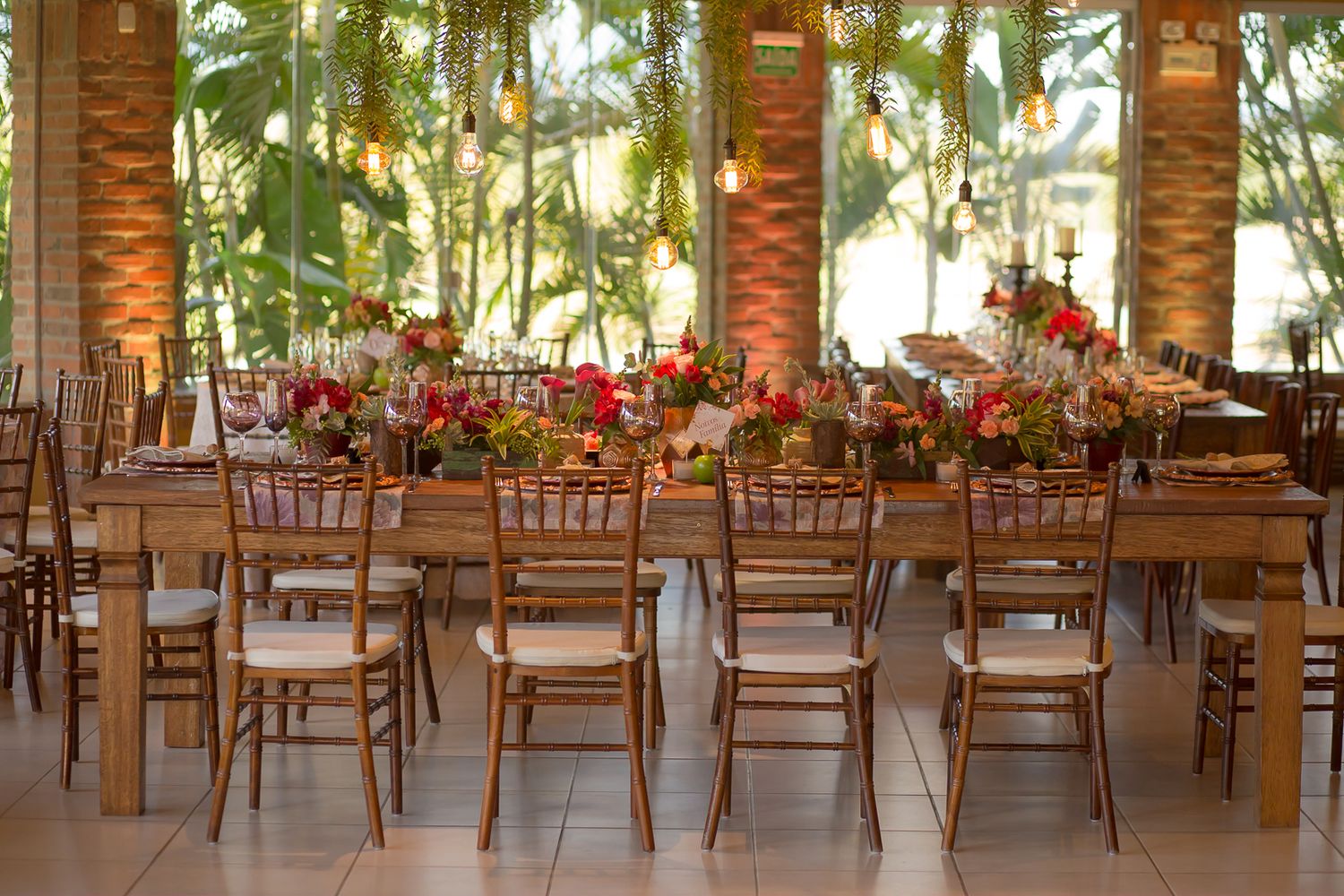 Wedding reception venue with wooden chairs and tables decorated with coral floral centerpieces.
