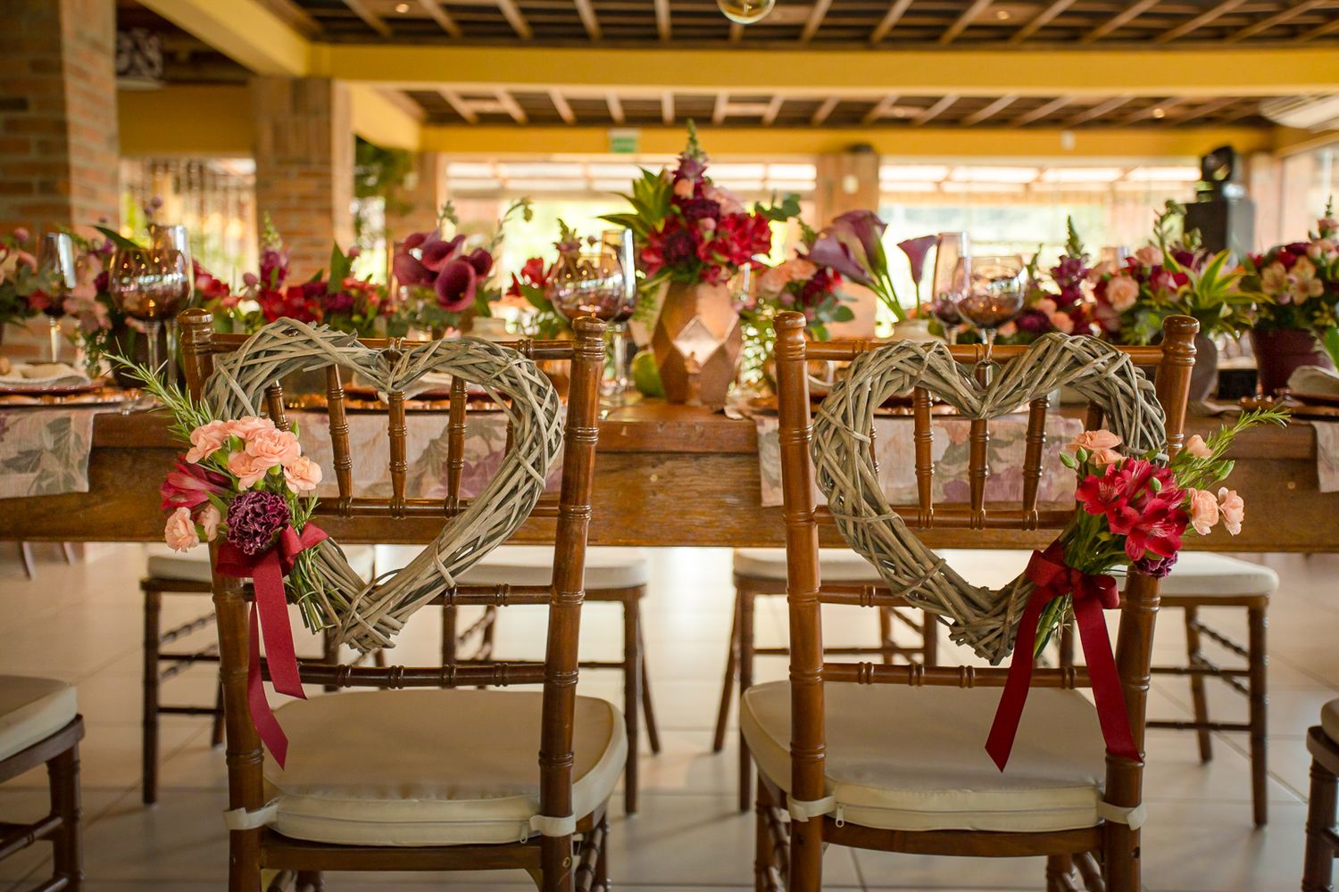 Elegant wedding reception chairs decorated with red floral arrangements and ribbons.