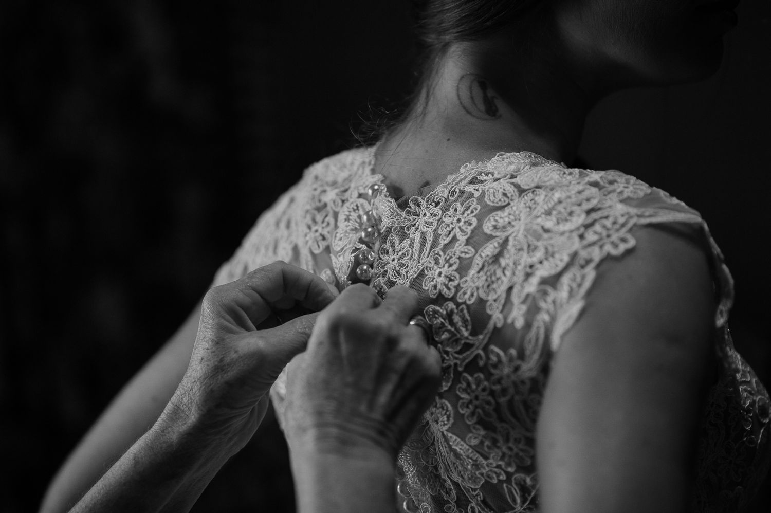 Close-up black and white image of hands fastening delicate lace buttons on a wedding dress.