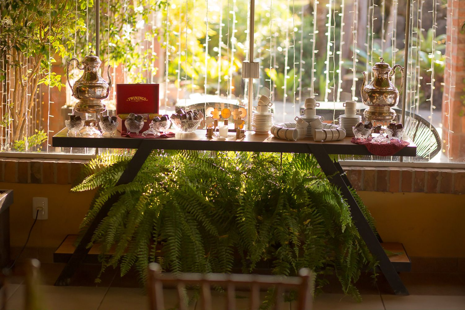 Elegant dessert table setup with glass stands and decor in warm sunlight.