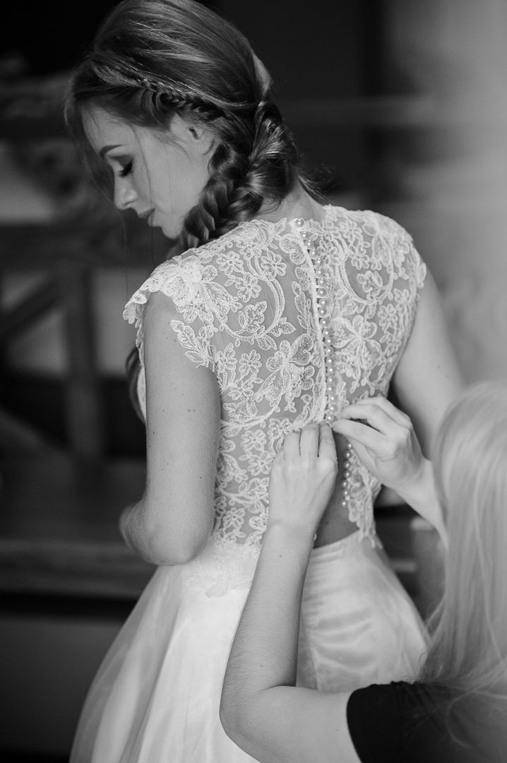 Black and white photo showing intricate lace detail on back of wedding gown during dressing.