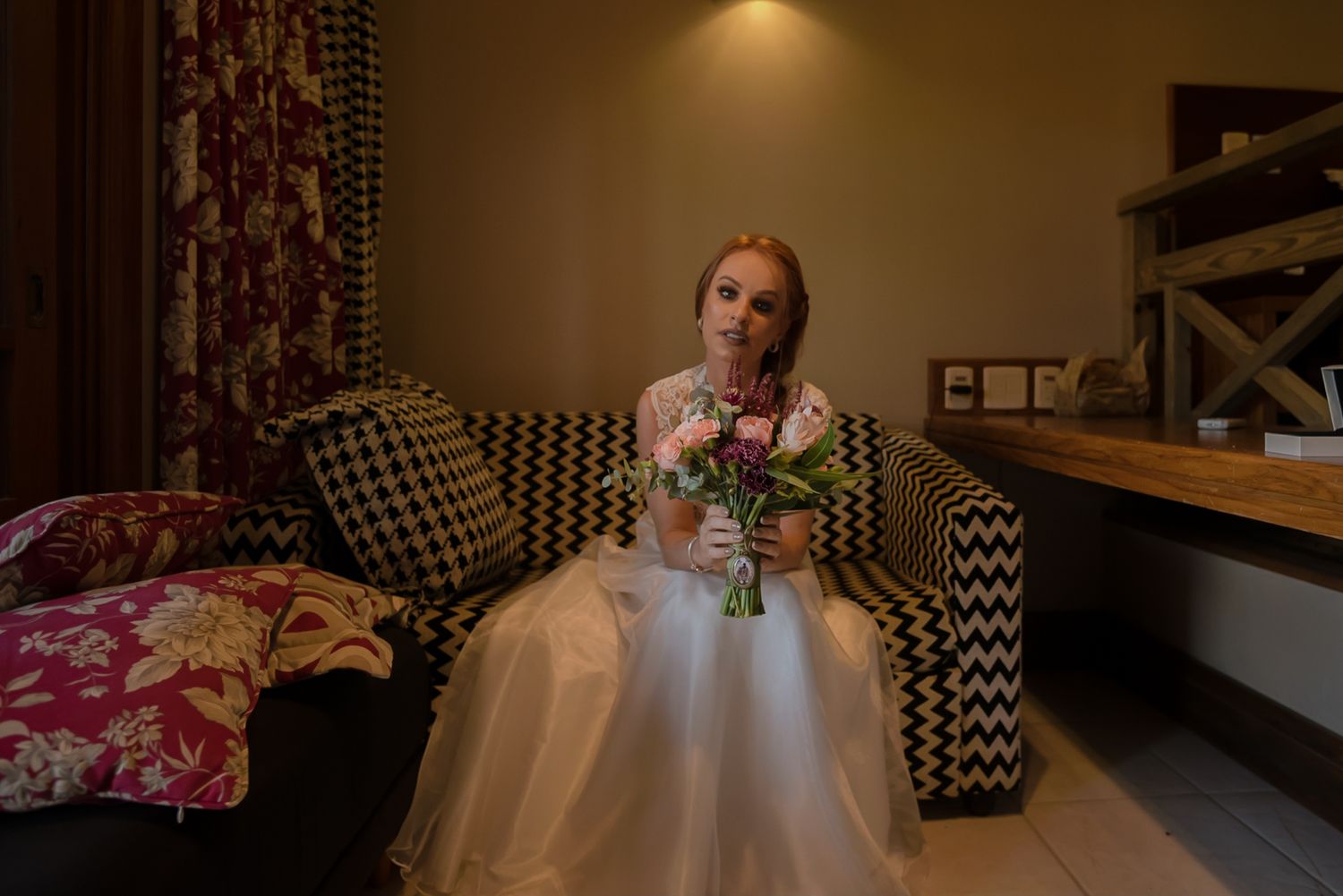 Interior shot of someone seated on patterned chair holding floral bouquet.