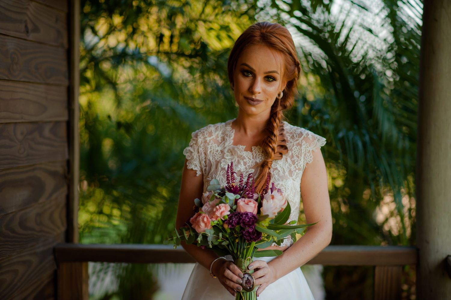 Sunlit outdoor portrait with person holding vibrant mixed flower bouquet on wooden porch.