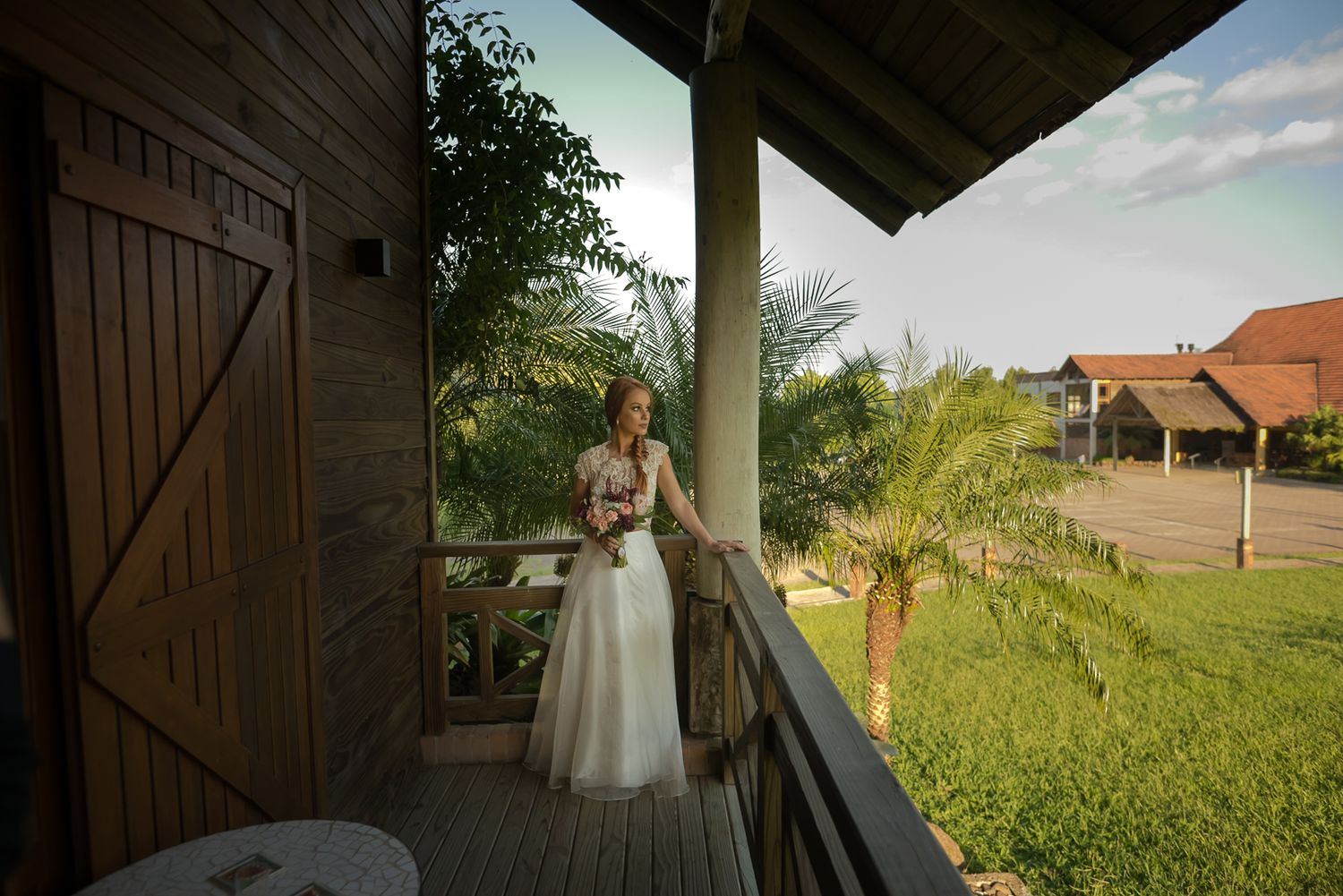 A scenic view of a rustic wedding venue's covered porch with palm trees and buildings in the background.