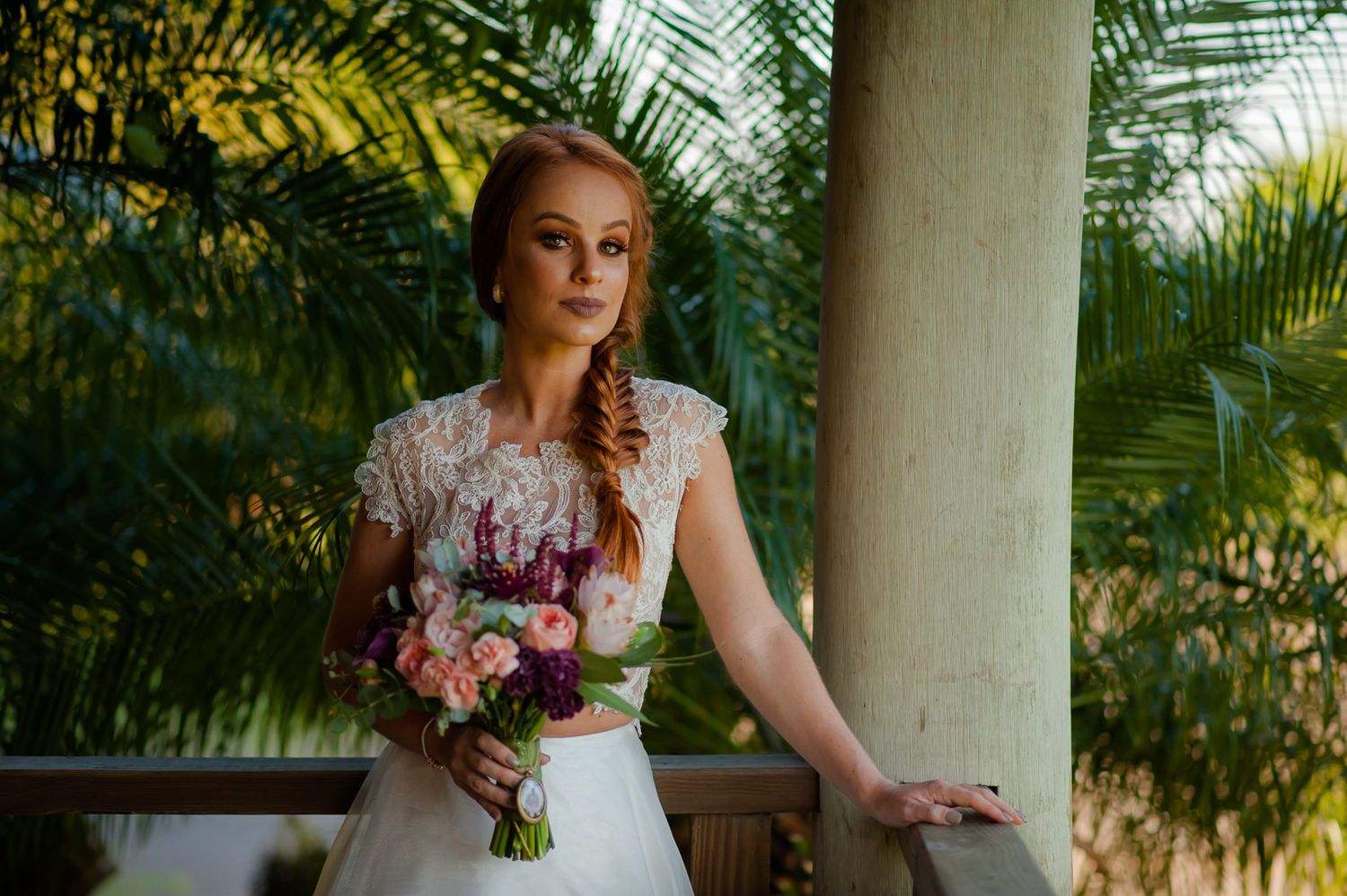 An elegant white lace wedding dress complemented by a colorful bouquet against a tropical backdrop.
