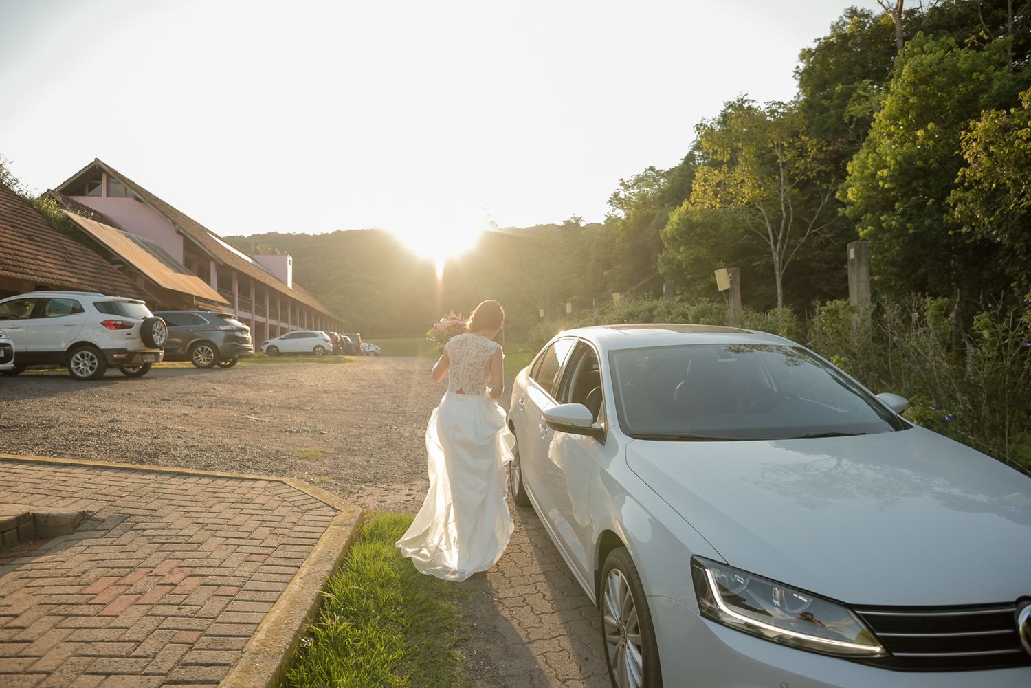 A white wedding dress silhouetted against golden sunset light in a parking area.
