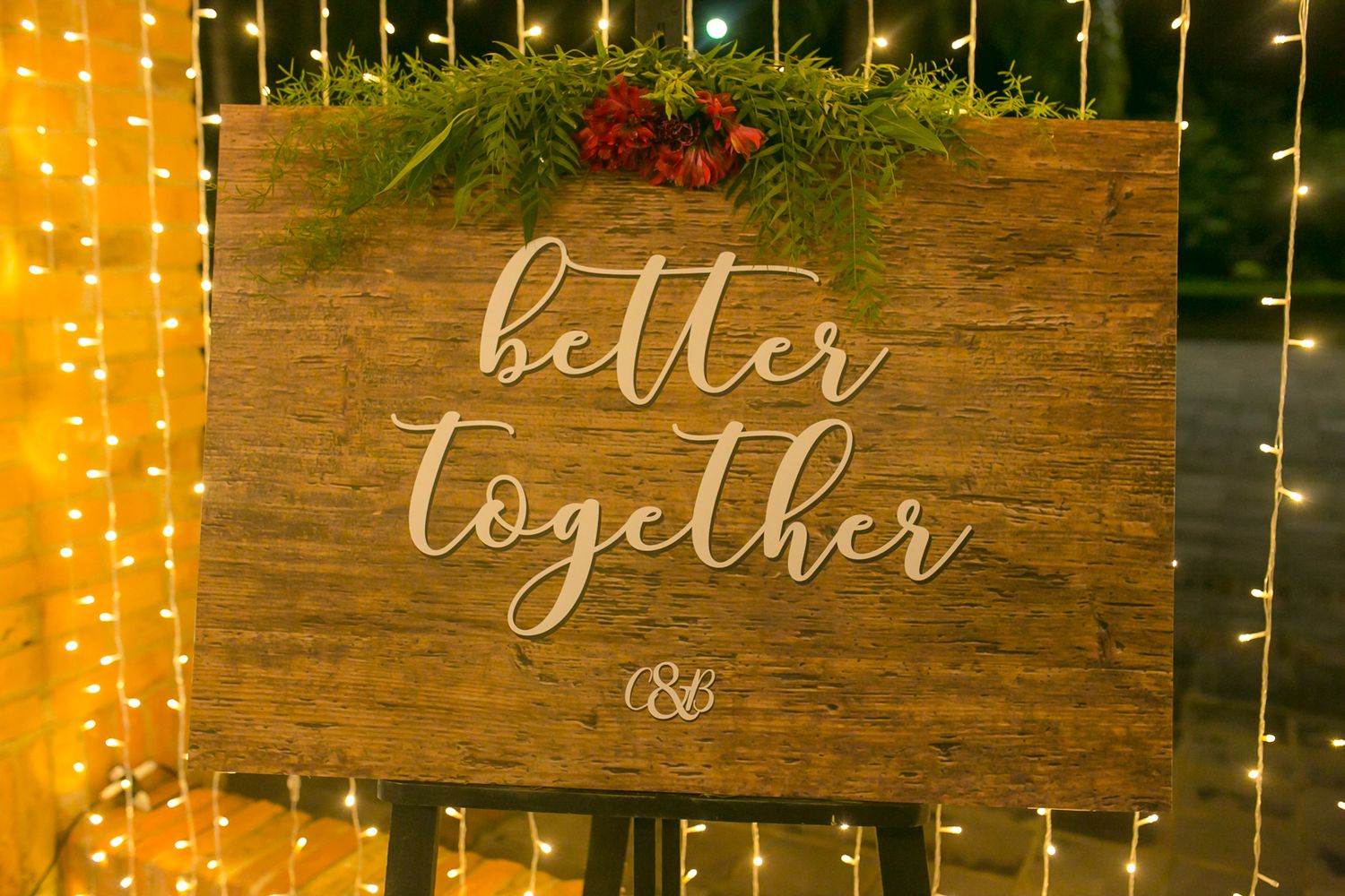 Rustic wooden wedding sign reading 'better together' illuminated by string lights.