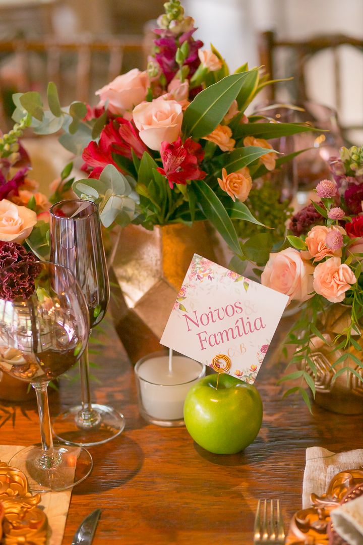 Wedding table arrangement with peach roses, a green apple, and a name card in Spanish.