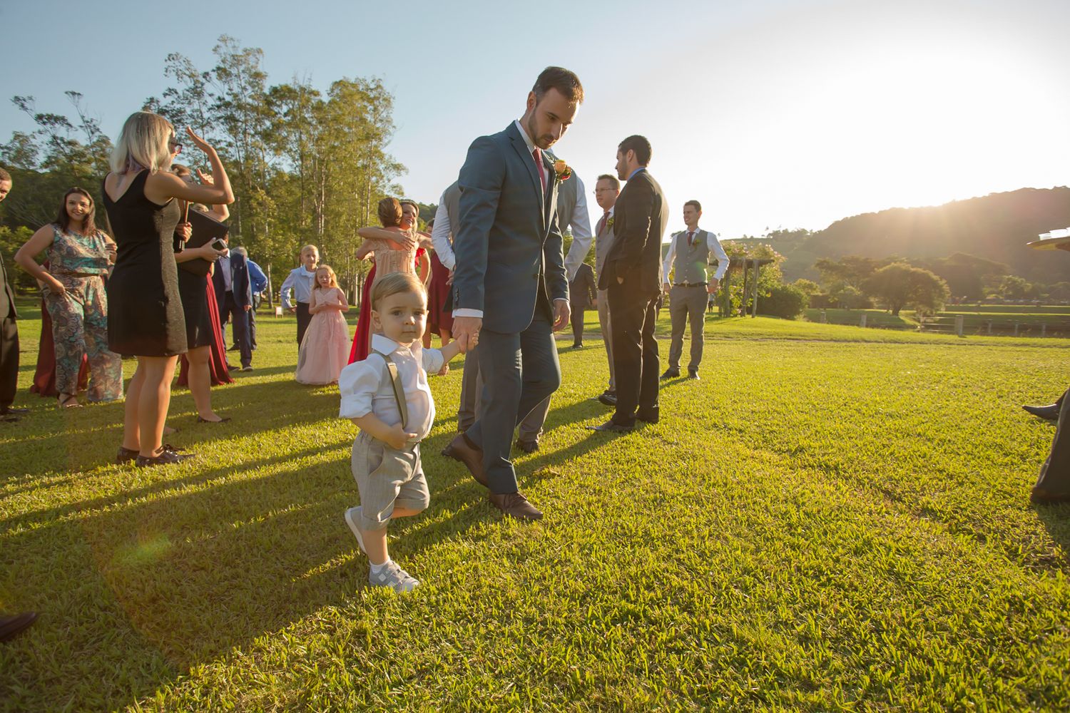 Wedding guests gather on a sunlit lawn during an outdoor celebration at sunset.
