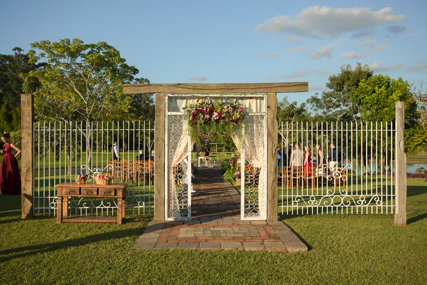 Elegant wedding archway with white drapes and floral decorations stands on a manicured lawn.