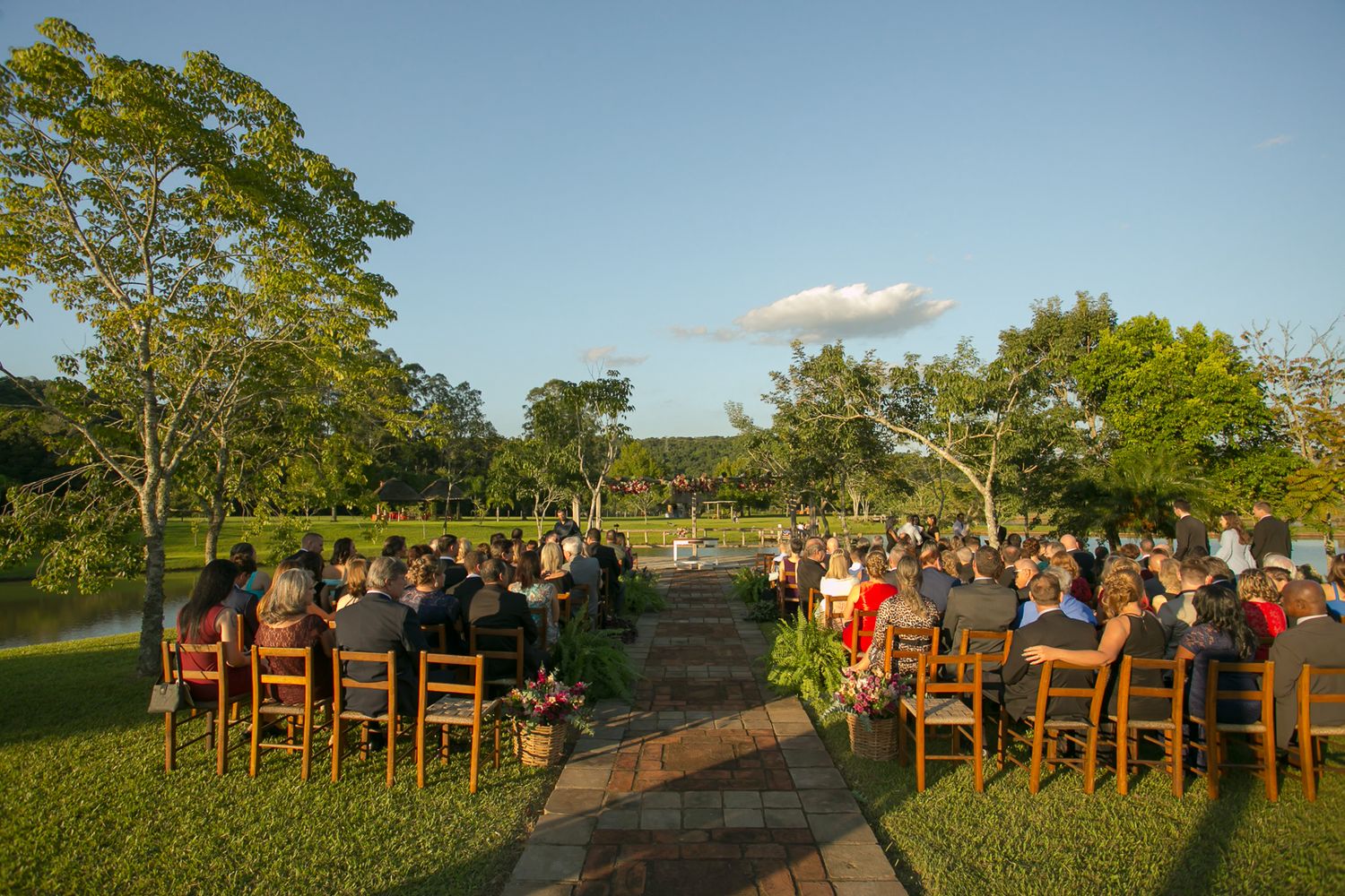 Wooden chairs line pathway for outdoor wedding ceremony under blue sky.