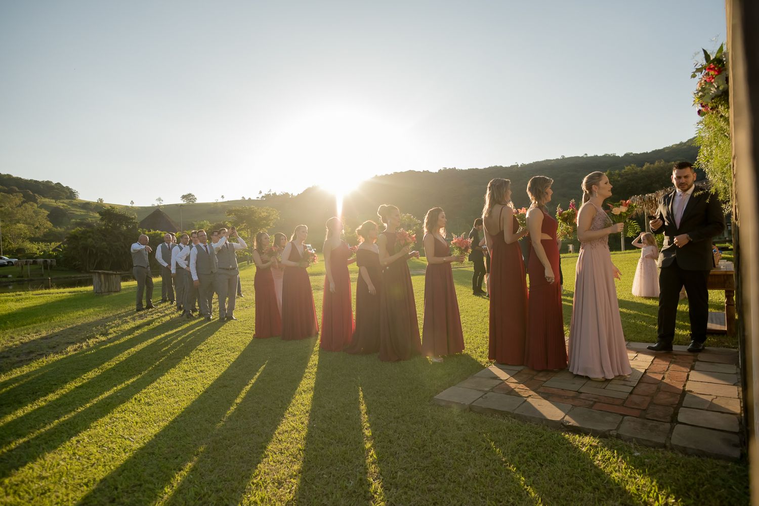 Wedding party poses on garden path during golden hour creating dramatic shadows.