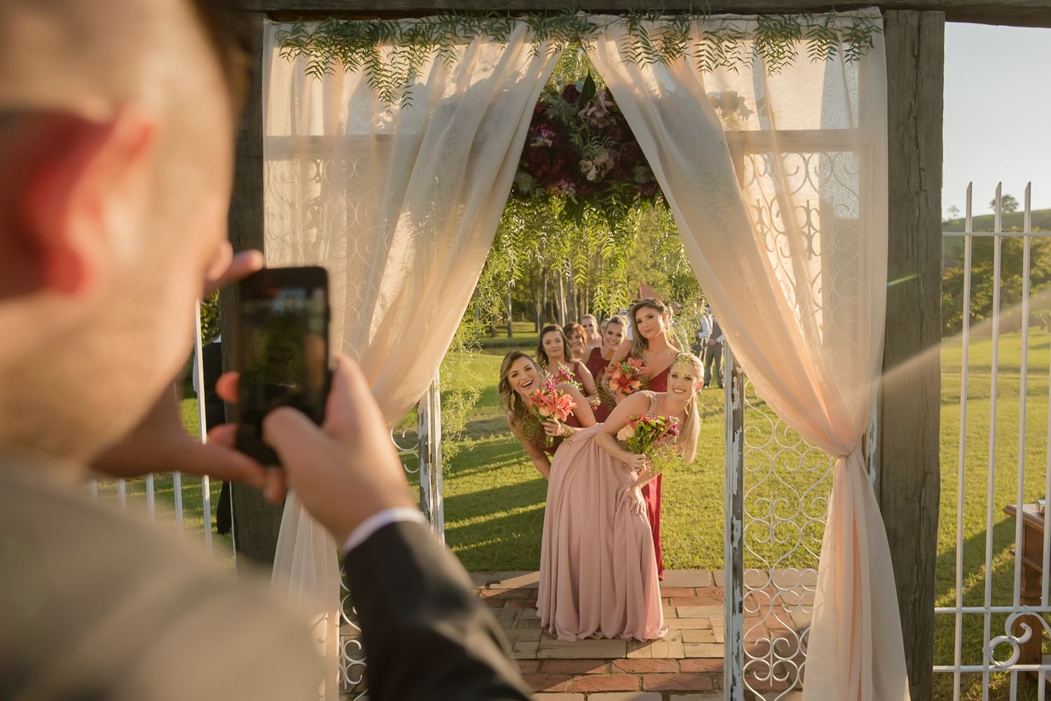 Guest captures photo under decorated wedding arch during outdoor ceremony.