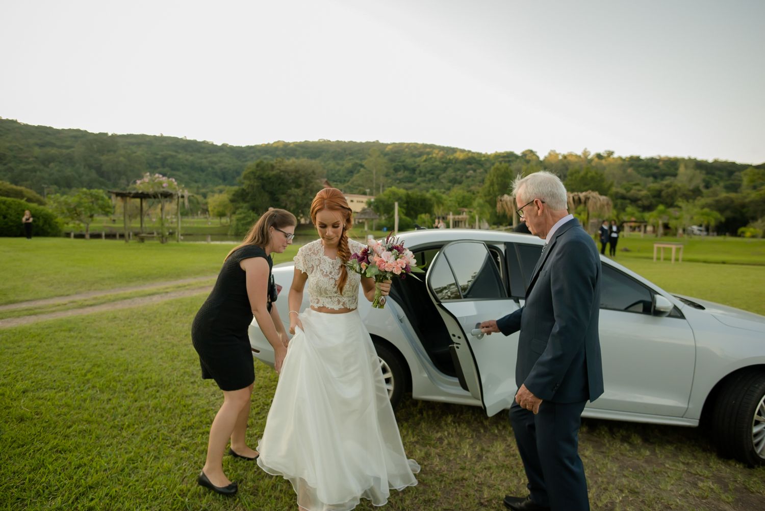Arriving at outdoor wedding venue in white car on grassy field.