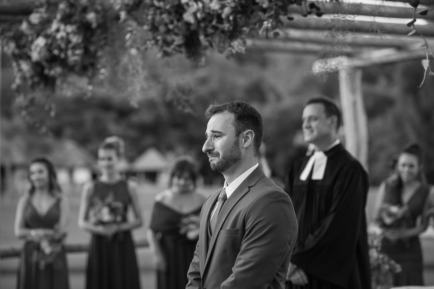 Black and white portrait during outdoor ceremony with attendants in background.