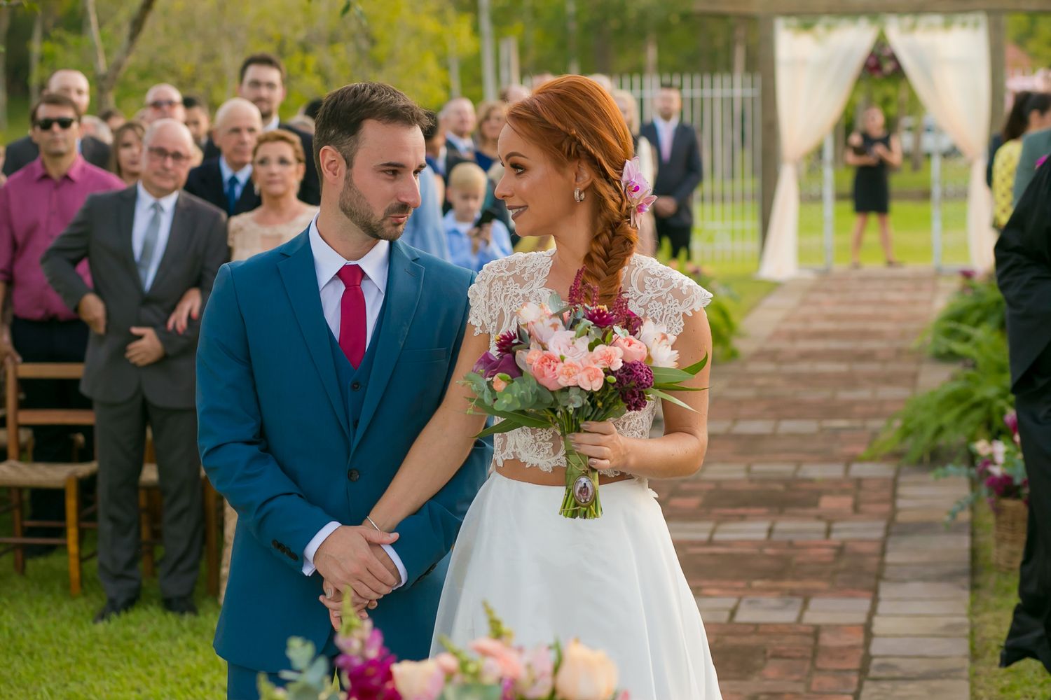 Couple shares emotional moment during garden wedding ceremony with guests looking on.