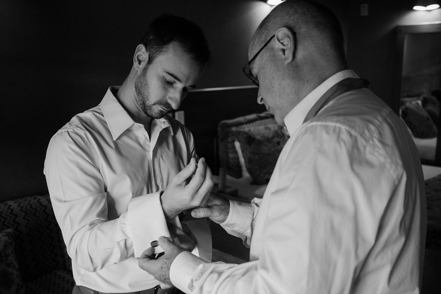 Two men in white dress shirts prepare for a formal event in a black and white photograph.