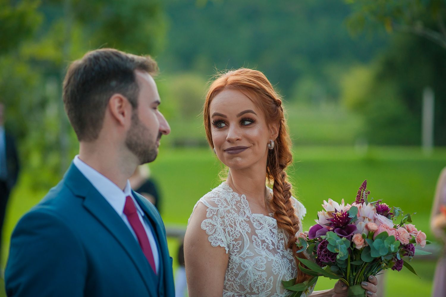 Outdoor wedding portrait with lush green background and vibrant floral bouquet.
