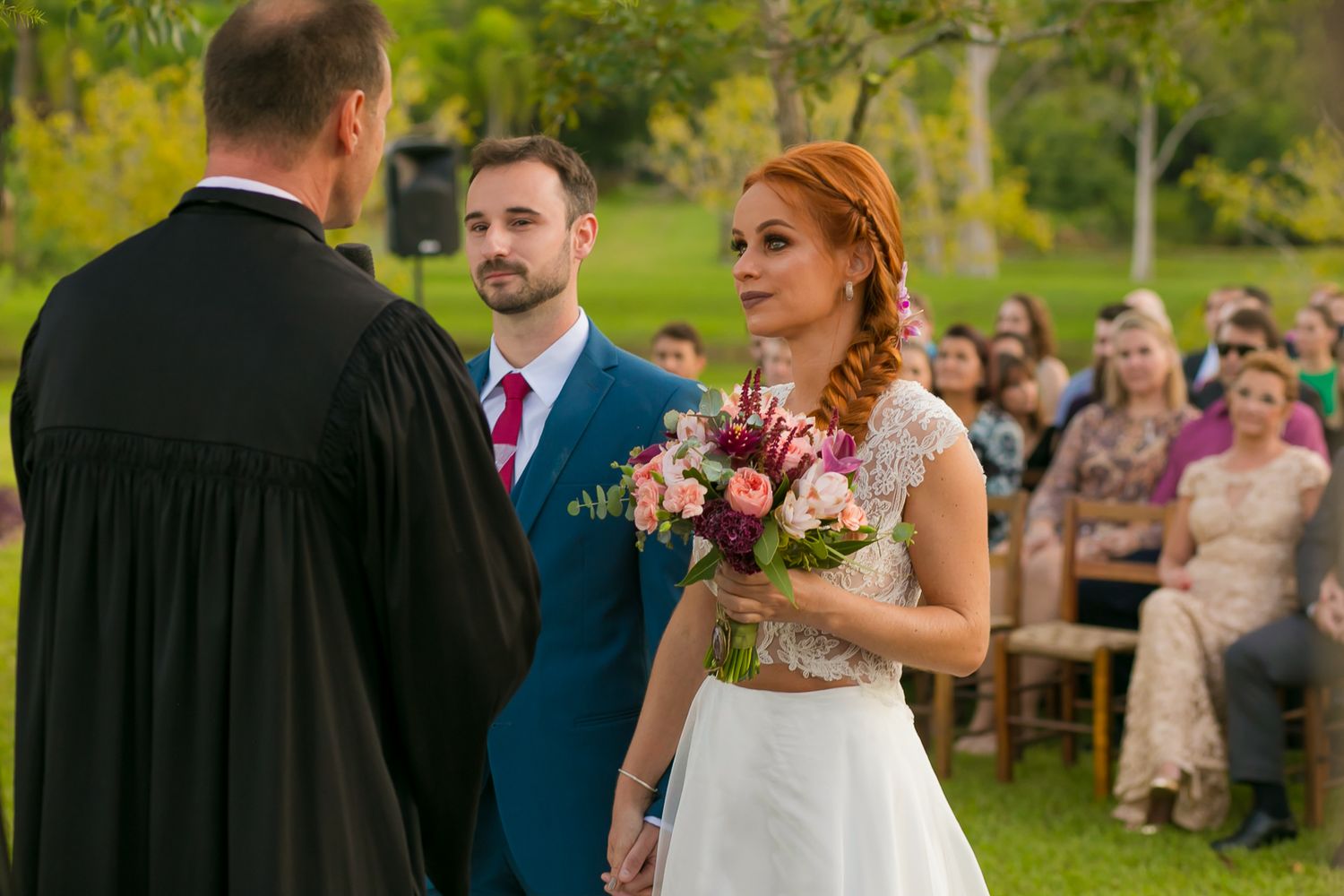 Wedding ceremony in progress with guests visible in background under natural lighting.