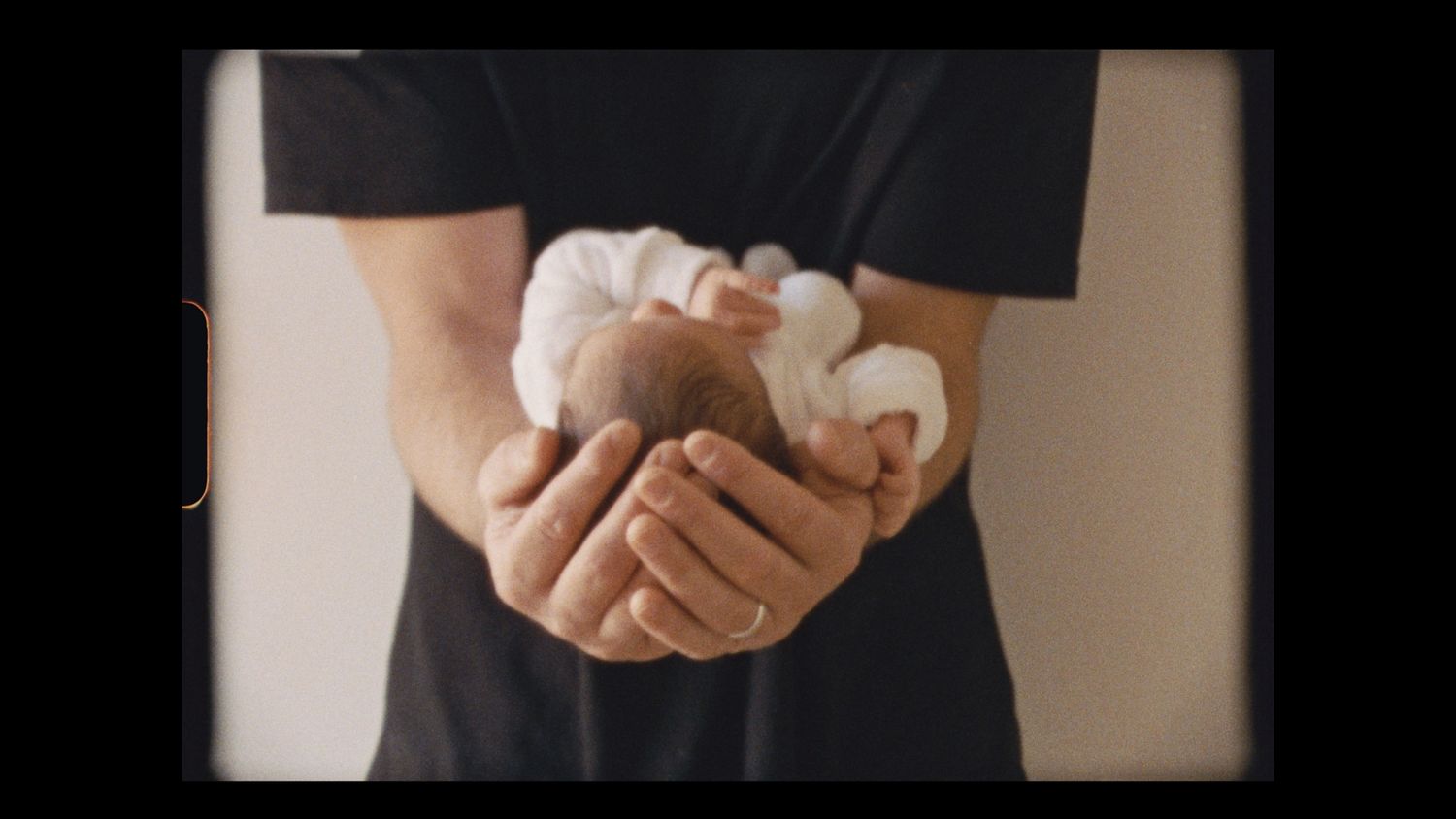 super 8 still of Dad holding newborn baby in his arms, his big hands around their little head, Anglesea, Victoria