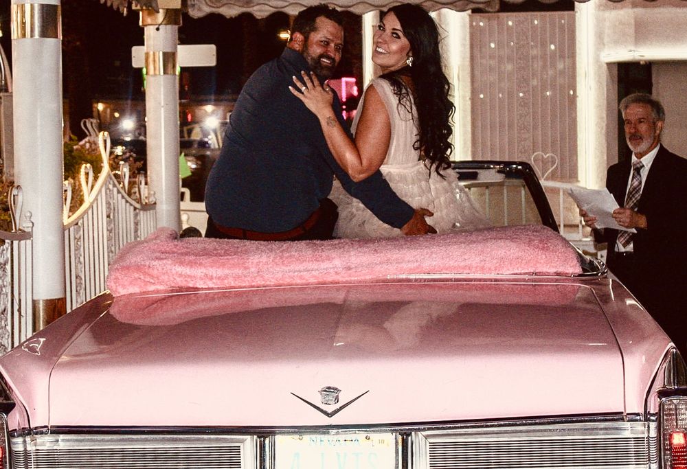 Couple posing in a pink vintage Cadillac convertible at a Las Vegas wedding chapel at night.