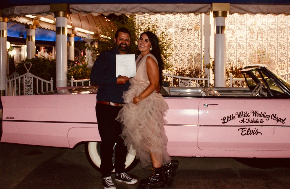 Couple posing in front of a pink Elvis-themed Little White Wedding Chapel car in Las Vegas.