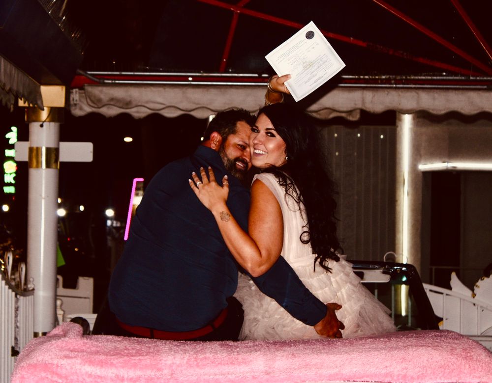 Joyful bride hugging groom while holding marriage certificate at outdoor wedding celebration at night.