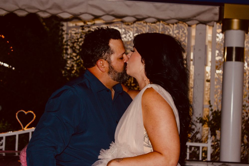 Couple sharing a romantic kiss at their wedding reception under a decorated outdoor tent at night.