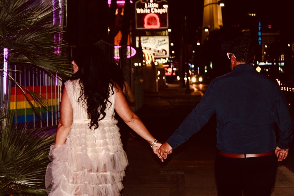 Newlywed couple holding hands walking at night on Las Vegas Strip in wedding attire.