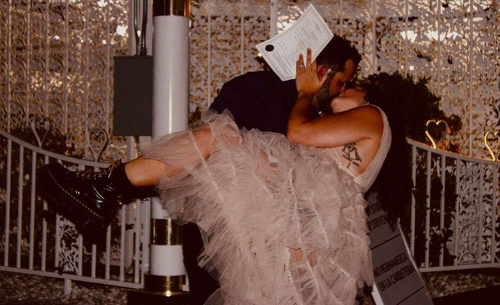 Bride in pink tulle gown dips during wedding reception dance near decorative backdrop.
