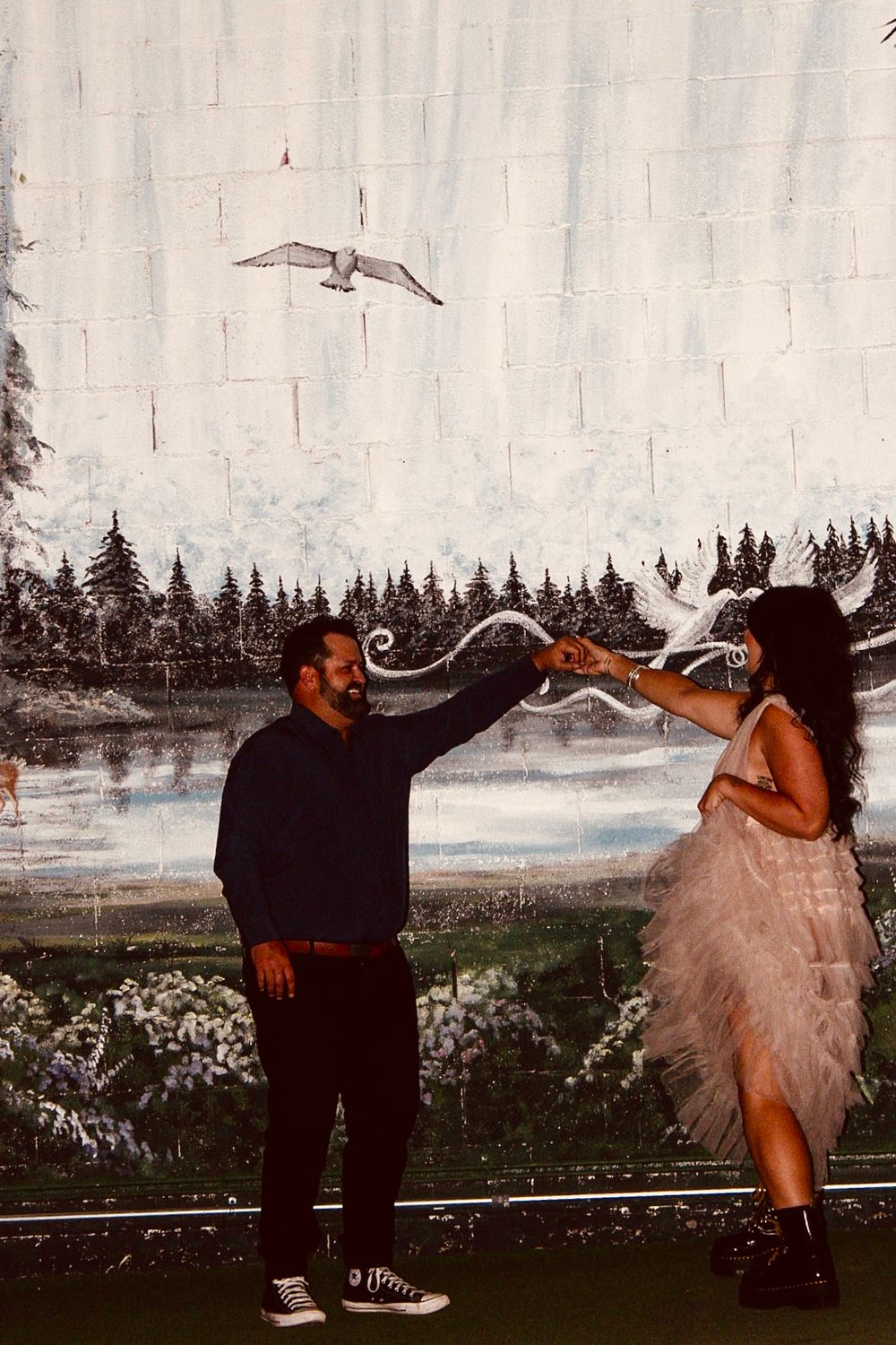 Couple shares a romantic hand-touch moment in front of a scenic nature mural at a Las Vegas wedding venue.