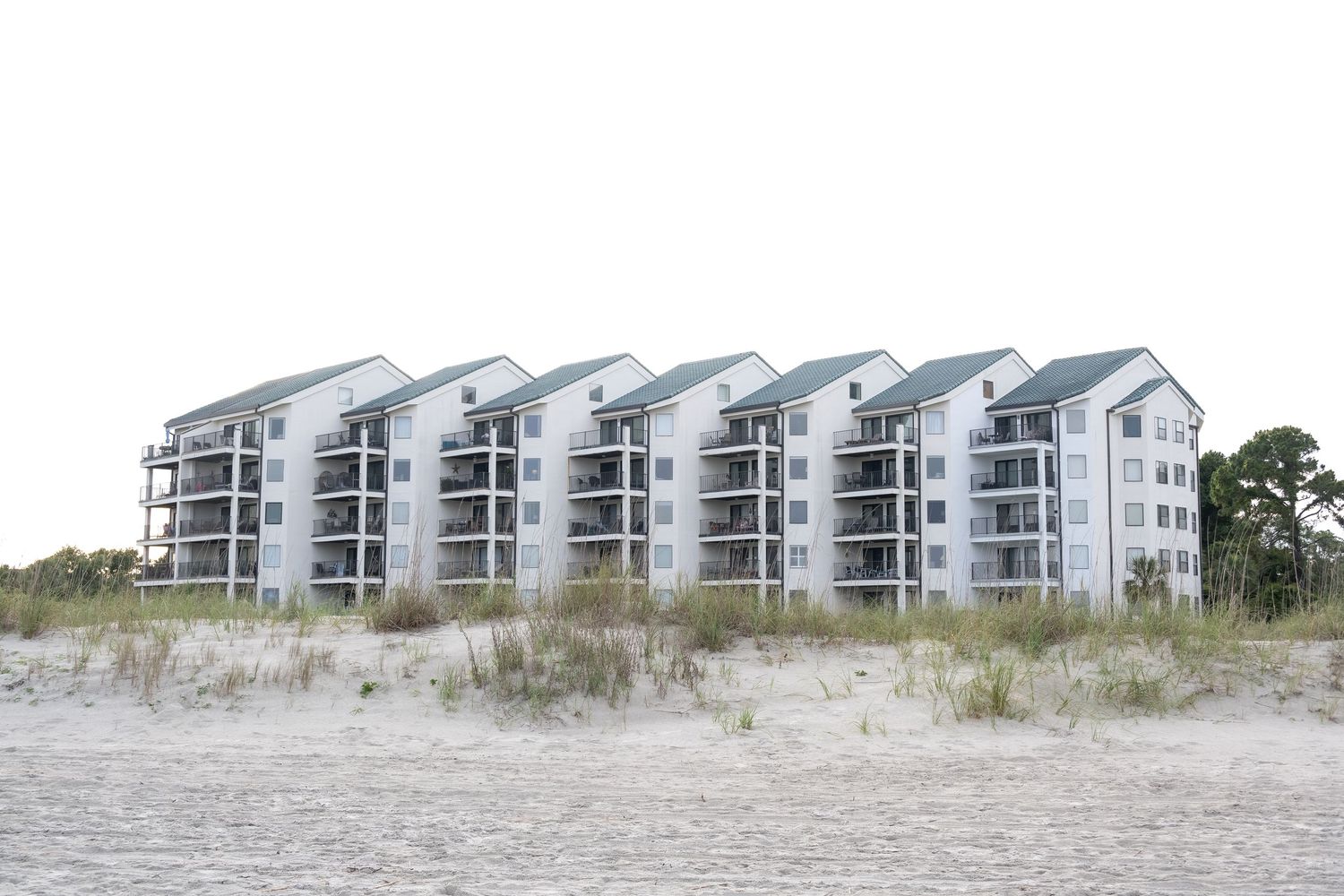 Row of white beach condominiums overlooking sandy dunes.