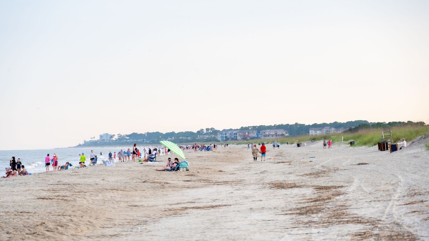 Wide sandy beach with scattered beachgoers and coastal buildings in distance.