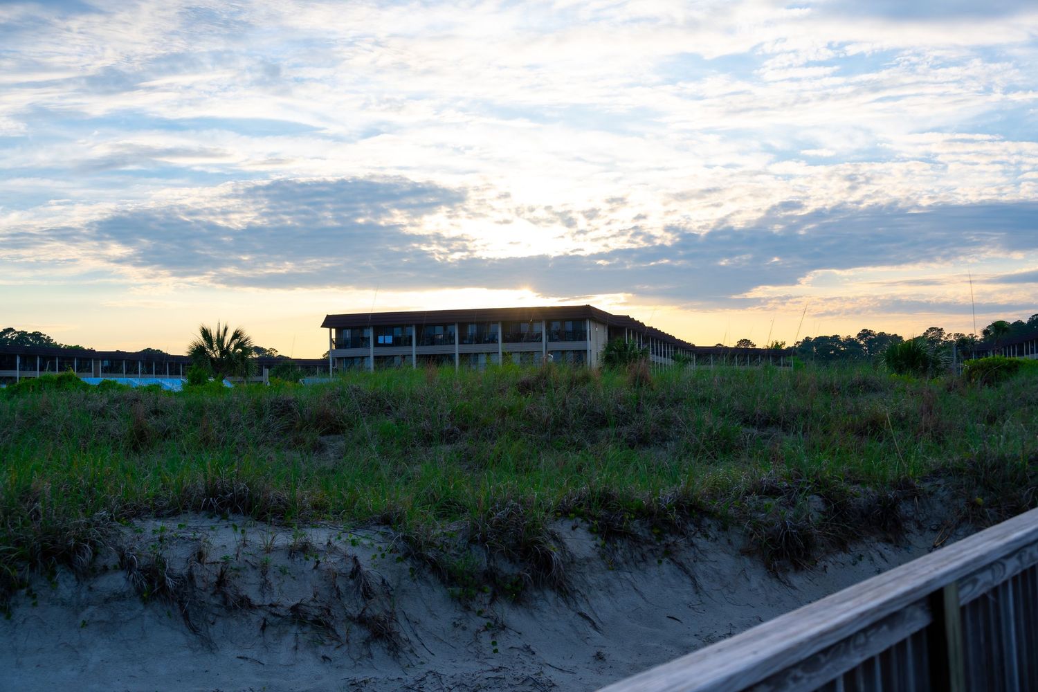 Coastal building sits atop sand dunes at sunset with dramatic cloudy sky.