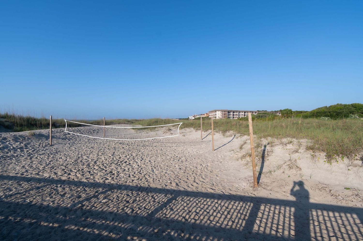 Sandy beach pathway with wooden fencing and shadows stretching across white sand.