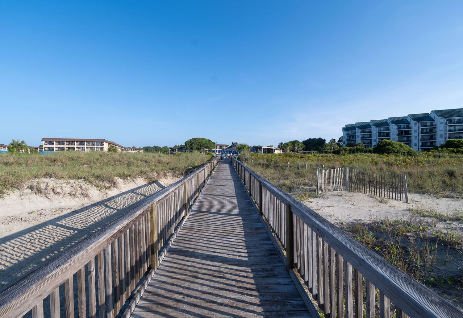 Long wooden boardwalk leads through coastal dunes to beachfront buildings.