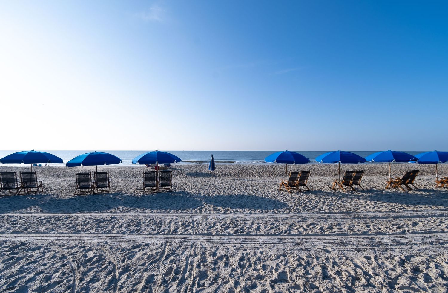Row of blue beach umbrellas and lounge chairs line the sandy shoreline.