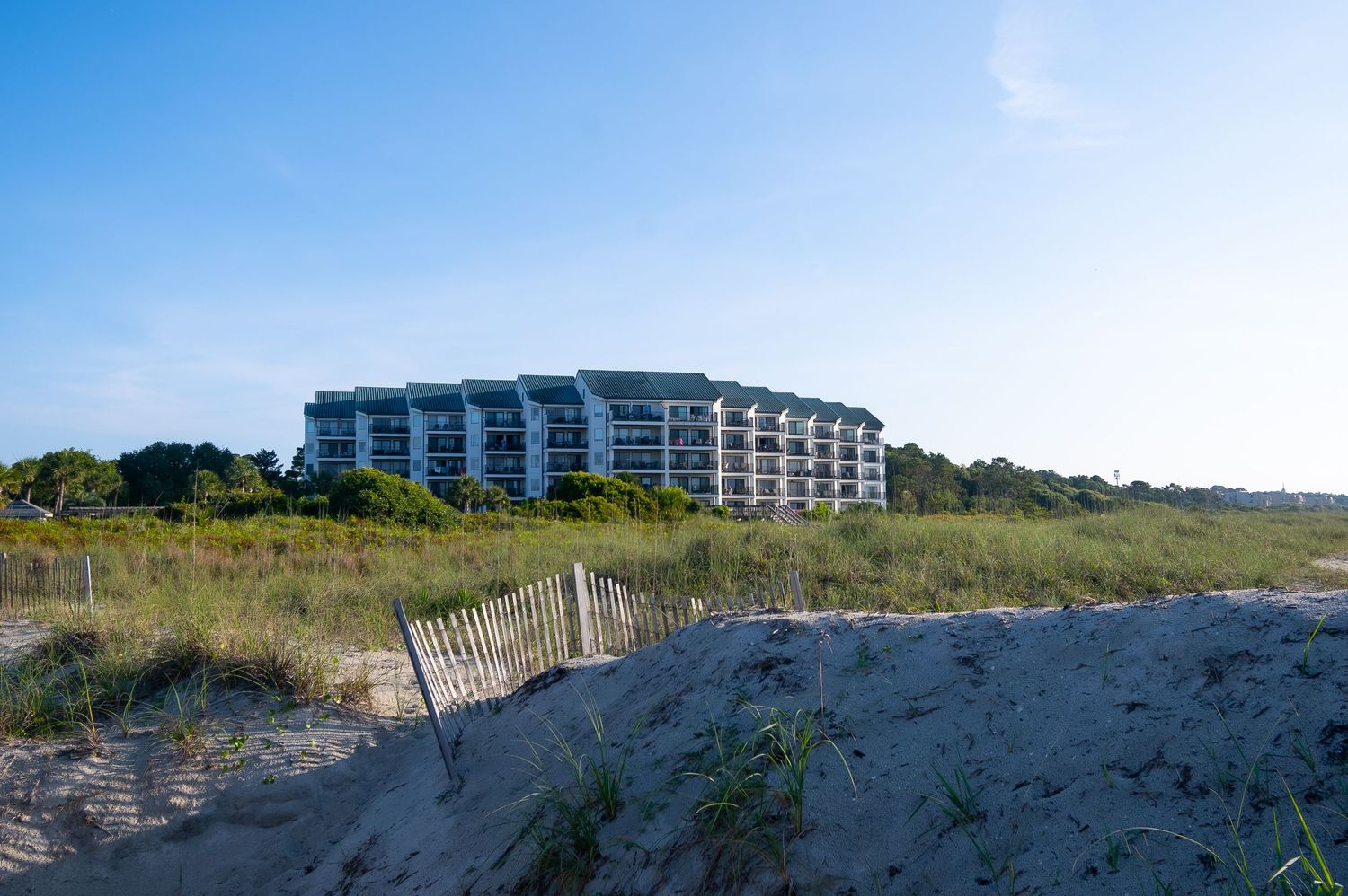 Modern beachfront hotel rises above coastal dunes under clear blue sky.