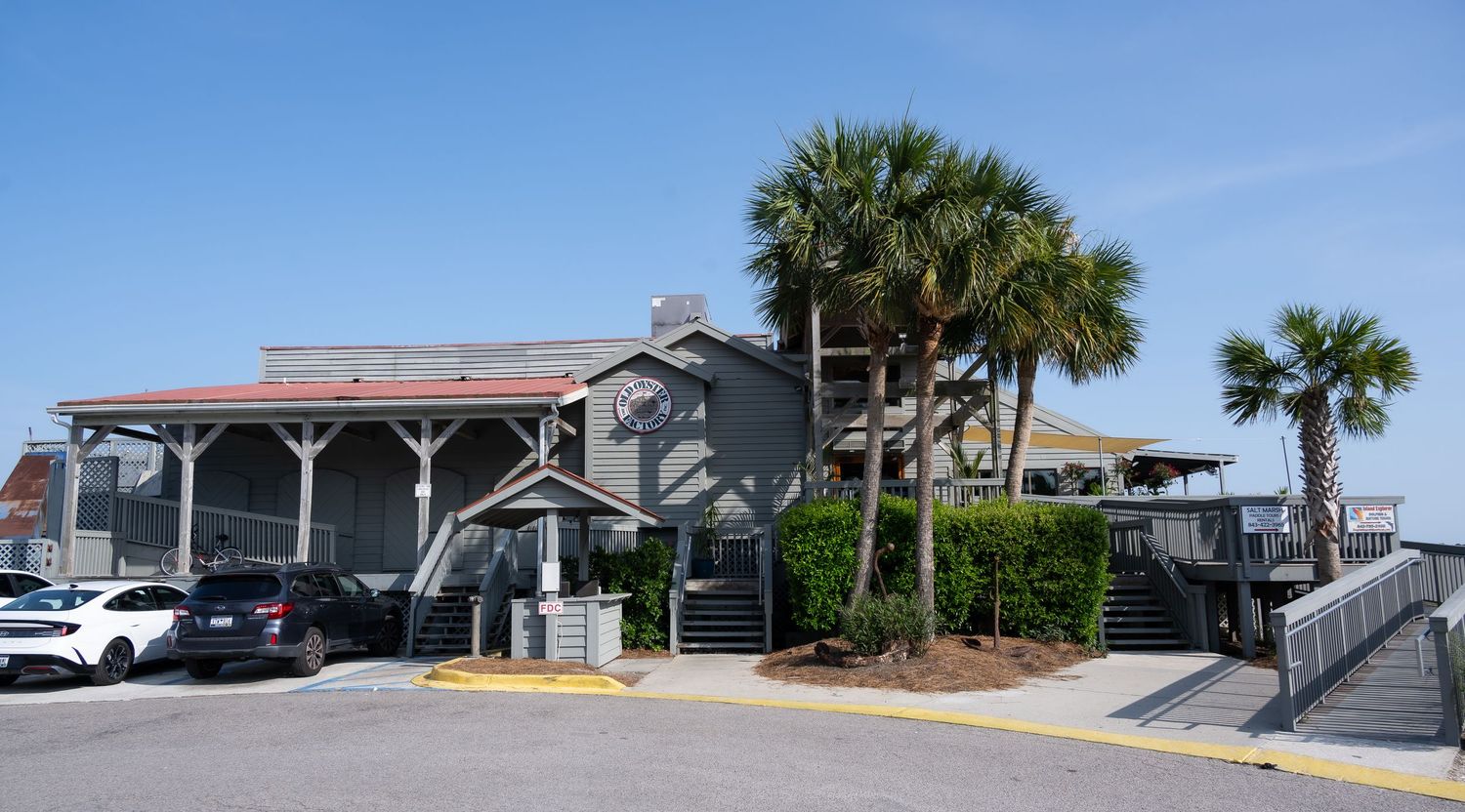 Gray coastal restaurant building with palm trees and parking area.
