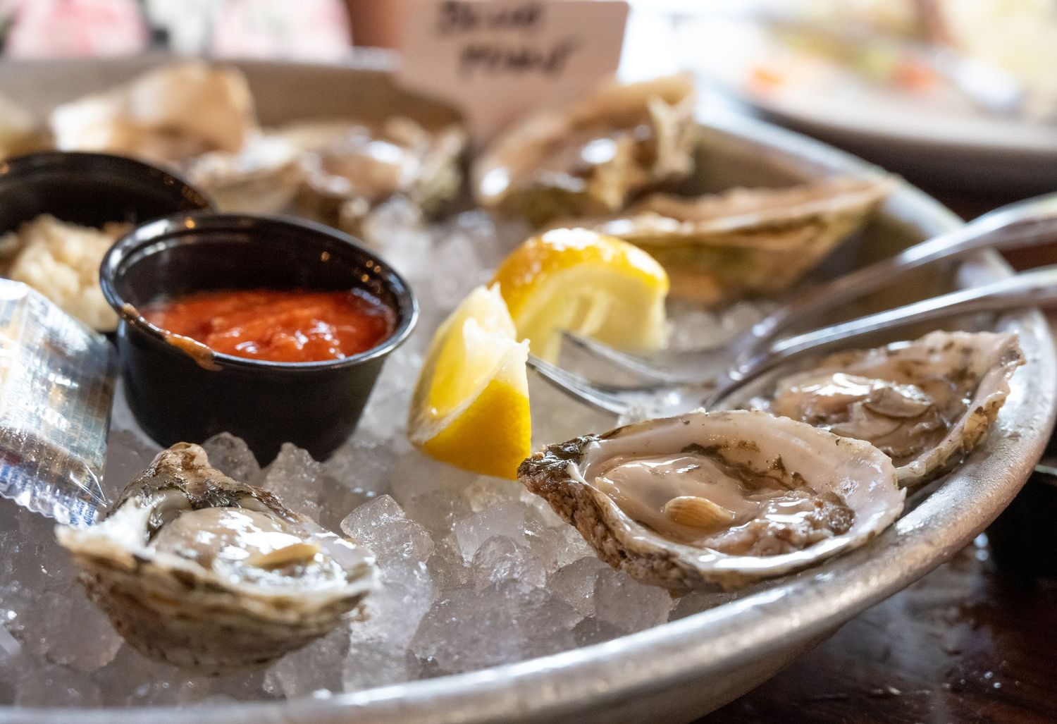 Fresh oysters served on ice with lemon wedges and cocktail sauce in dark bowl.