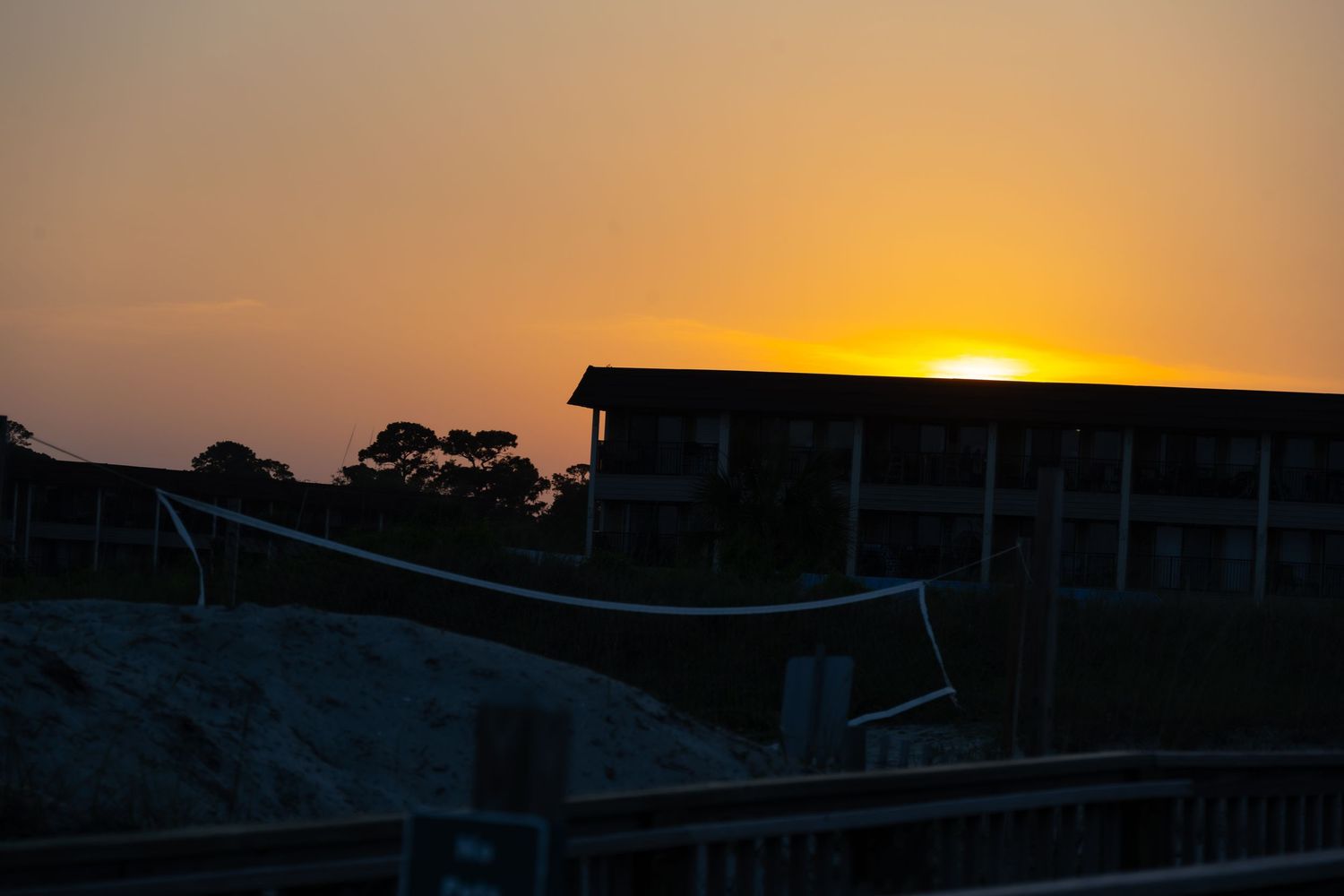 Dramatic orange sunset silhouettes coastal building structure against darkening sky.