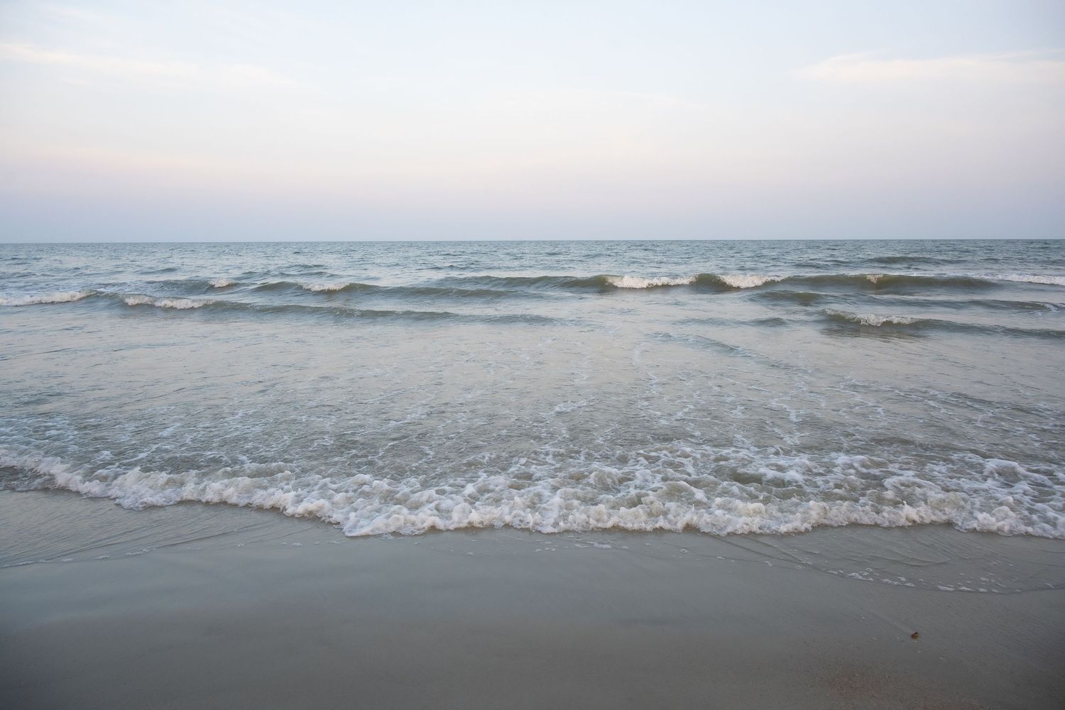 Gentle ocean waves rolling onto sandy beach at dusk with misty atmosphere.