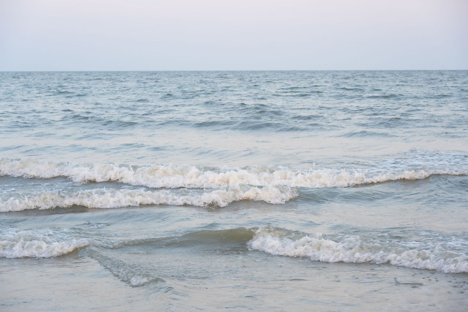 Peaceful seascape with soft waves breaking on beach under pale sky.