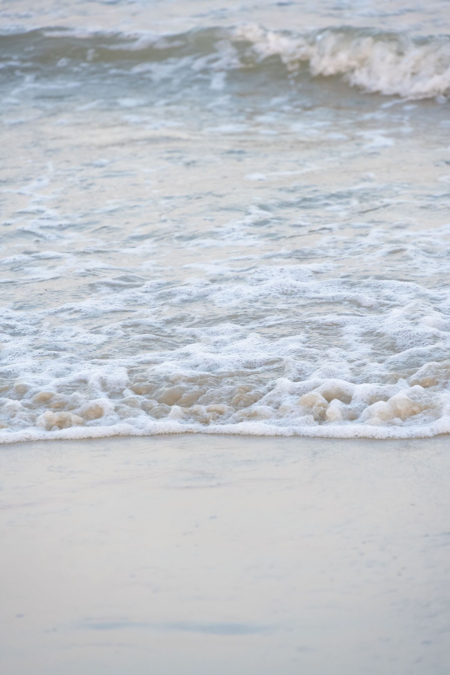 Gentle ocean waves washing up on a sandy beach with white foam in close-up view.