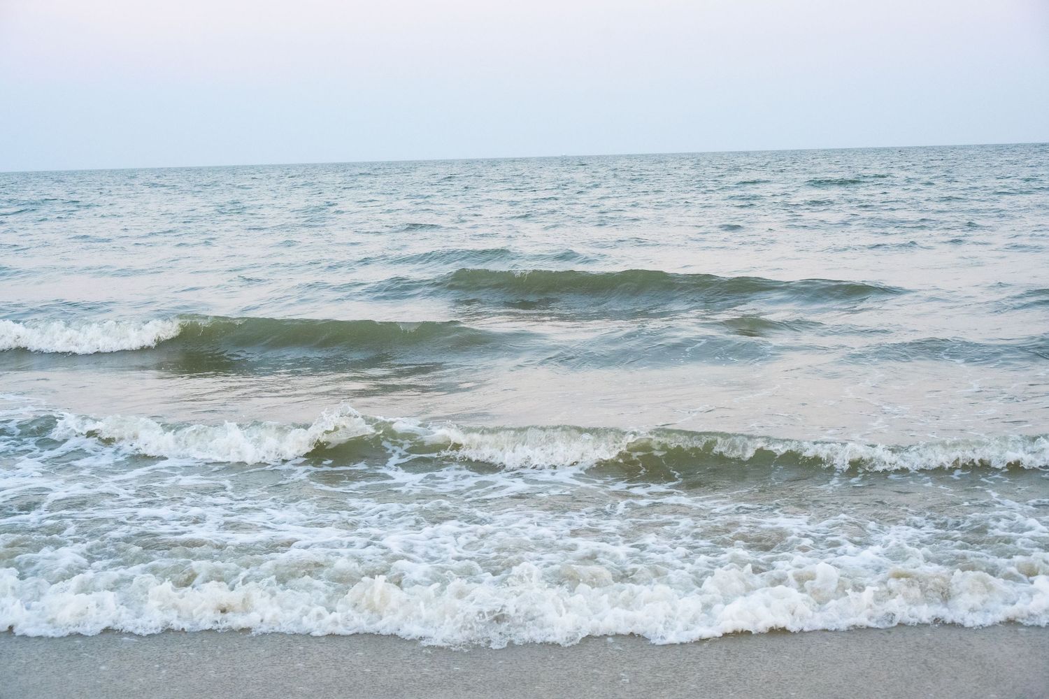 Ocean waves rolling onto the beach during a cloudy day.
