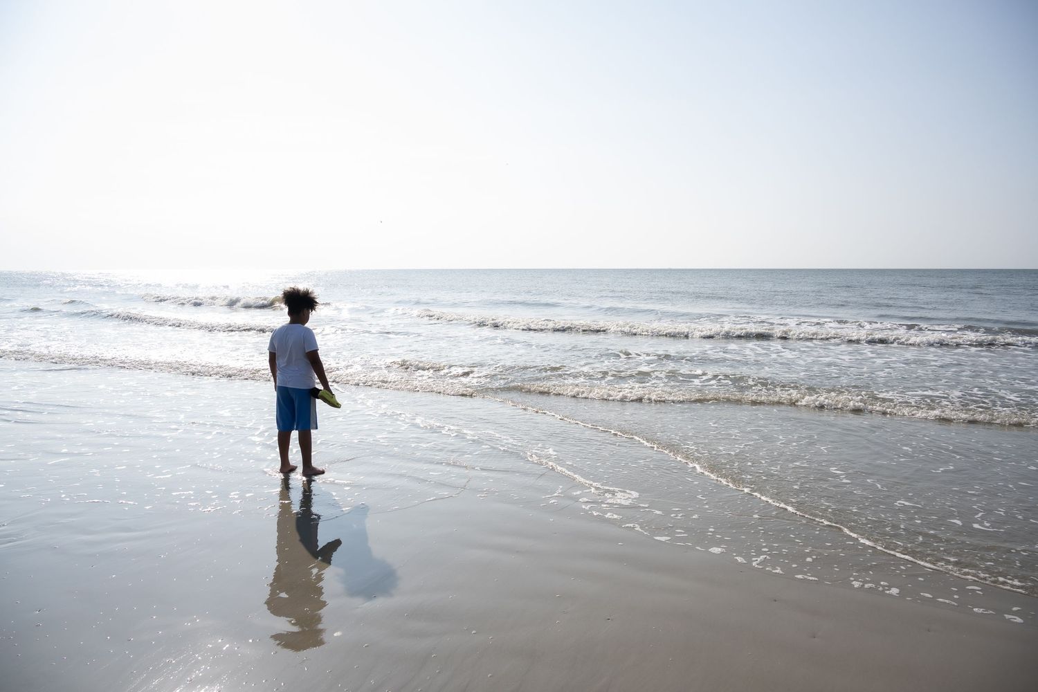 A silhouetted figure walking along the shoreline at the beach as waves roll in.