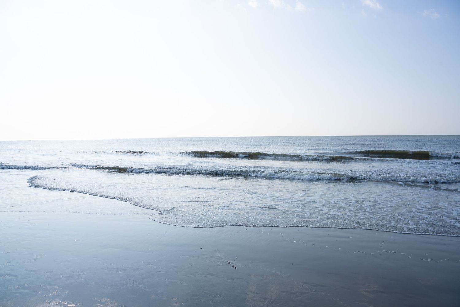 Gentle waves roll onto a peaceful beach shoreline under a bright blue sky.