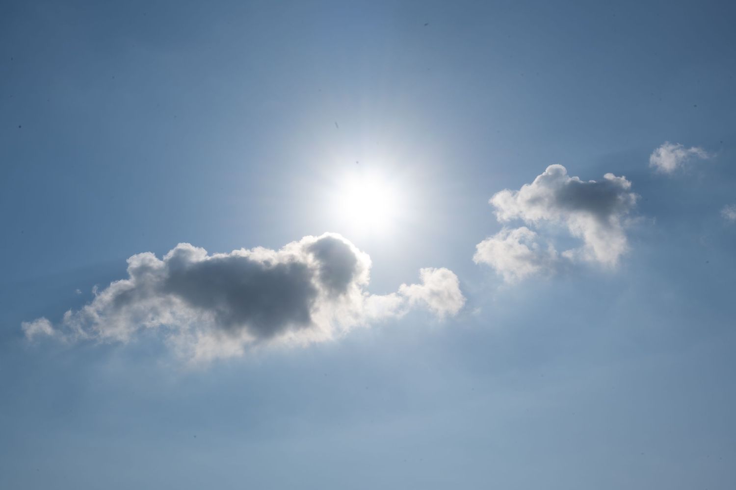 Bright sun peeks through white fluffy clouds in a vibrant blue sky.